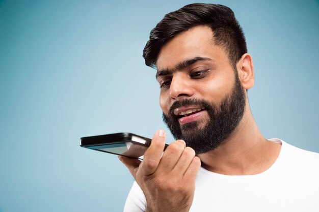 Nahaufnahmeporträt des jungen indischen Mannes im weißen Hemd. Auf dem Handy sprechen, Sprachnachrichten aufzeichnen.