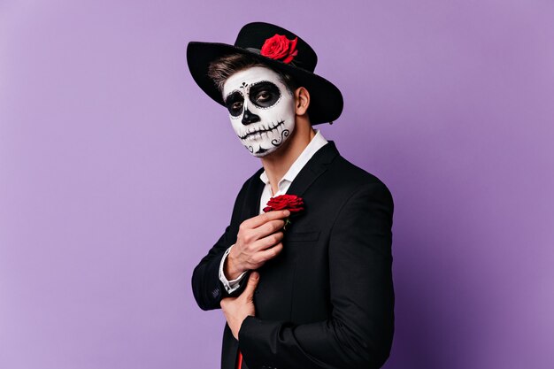 Nahaufnahmeporträt des Kerls im Halloween-Kostüm im mexikanischen Stil, ergänzendes Outfit mit roter Rose.