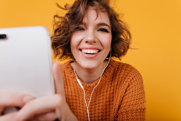 Nahaufnahmeporträt des lachenden weißen Mädchens, das Telefon für selfie verwendet