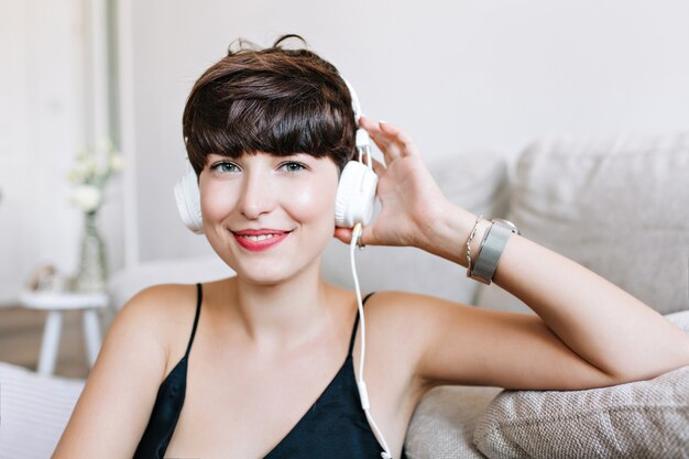 Nahaufnahmeporträt des leicht gebräunten lachenden Mädchens mit grauen Augen, die Musik genießen