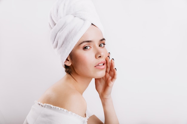 Nahaufnahmeporträt des Modells im Handtuch auf Kopf. Mädchen ohne Make-up berührt sanft ihr Gesicht.