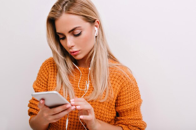 Nahaufnahmeporträt des ruhigen blonden weiblichen Modells mit eleganter Make-up-SMS am Telefon