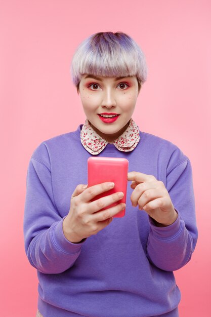 Nahaufnahmeporträt des schönen dollischen Mädchens mit dem kurzen hellen violetten Haar, das lila Pullover trägt, der selfie über rosa Wand macht