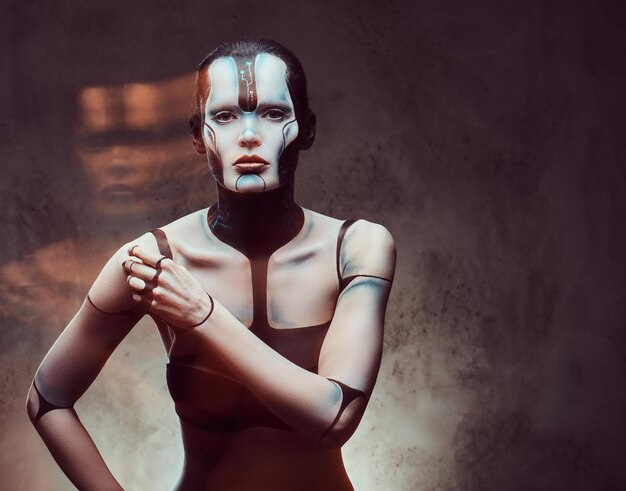 Nahaufnahmeporträt einer Cyberfrau mit kreativem Make-up mit Lichteffekt, die auf einem dunklen strukturierten Hintergrund aufwirft. Technologie und Zukunftskonzept.