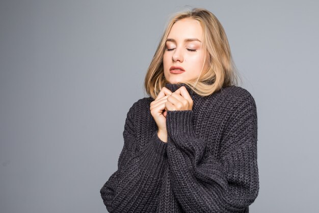 Nahaufnahmeporträt einer jungen glücklichen Frau im warmen Winteroutfit auf grauem Hintergrund