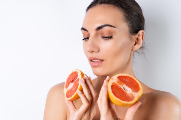 Nahaufnahmeporträt einer schulterfreien Frau mit perfekter Haut und natürlichem Make-up voller nackter Lippen, die frisches Zitrusvitamin C Grapefruitx9 halten