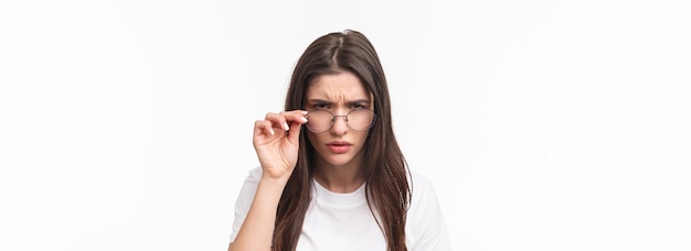 Kostenloses Foto nahaufnahmeporträt einer verdächtigen jungen ernsthaft aussehenden frau, die unter einer brille hervorschaut und perso blinzelt