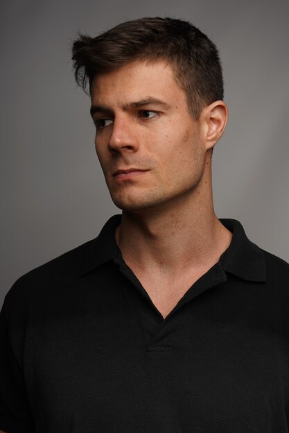 Nahaufnahmeporträt eines attraktiven Mannes in einem schwarzen T-Shirt gegen eine graue Wand
