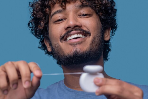 Nahaufnahmeporträt eines fröhlichen Inders, der den offenen Zahnseidebehälter in den Händen hält