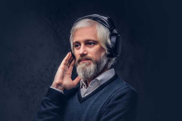 Nahaufnahmeporträt eines hübschen älteren Mannes, der Musik in den Kopfhörern hört. Lokalisiert einen dunklen Hintergrund.