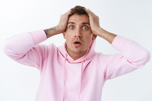 Nahaufnahmeporträt eines nervösen, in panik geratenen blonden, gutaussehenden mannes in rosa hoodie, kopf greifen, ängstlich nach luft schnappen, angst oder alarm wegen einer schrecklichen situation haben