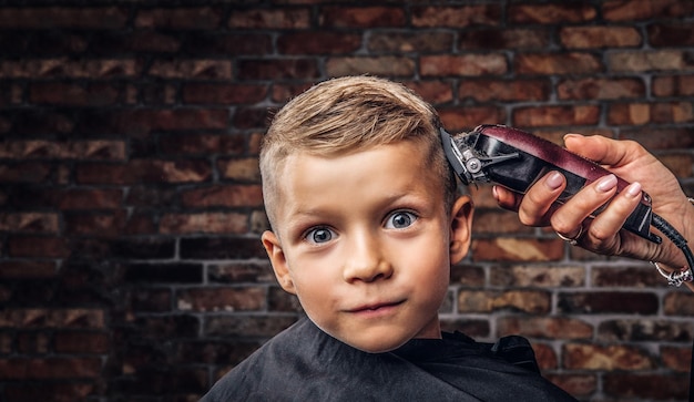 Nahaufnahmeporträt eines netten lächelnden Jungen, der Haarschnitt gegen die Backsteinmauer erhält.