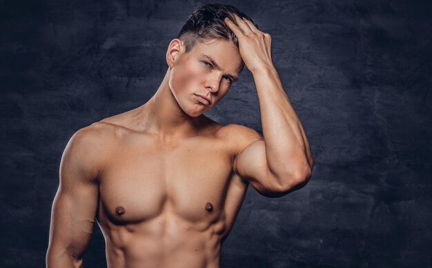 Nahaufnahmeporträt eines sexy, hemdlosen jungen Mannmodells mit muskulösem Körper und stylischem Haarschnitt, das in einem Studio posiert. Getrennt auf einem dunklen Hintergrund.