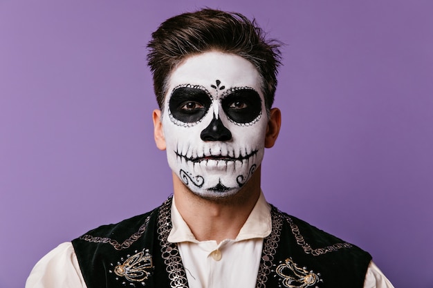 Nahaufnahmeporträt von Brunet mit Gesicht gemalt für Halloween. Braunäugiger Mann im weißen Hemd