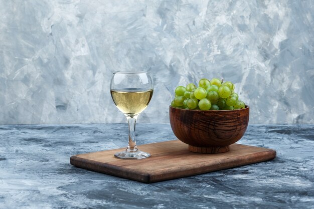 Nahaufnahmeschale der weißen Trauben, Glas Whisky auf Schneidebrett auf dunklem und hellblauem Marmorhintergrund. horizontal