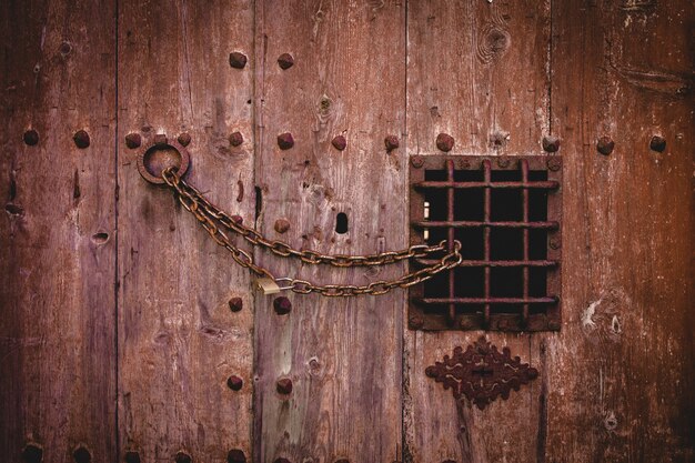 Nahaufnahmeschuss eines alten rostigen Kettenschlosses auf einer großen Holztür mit einem kleinen Metallzaun
