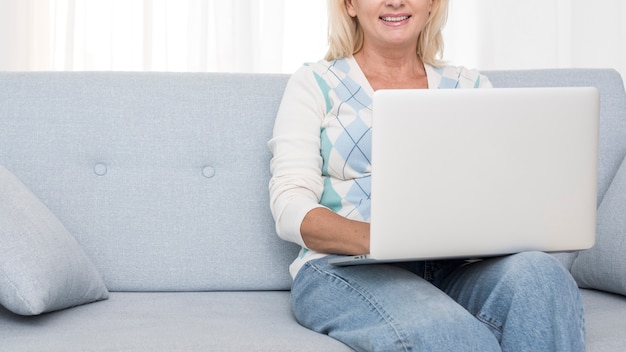 Nahaufnahmesmileyfrau mit Laptop auf der Couch