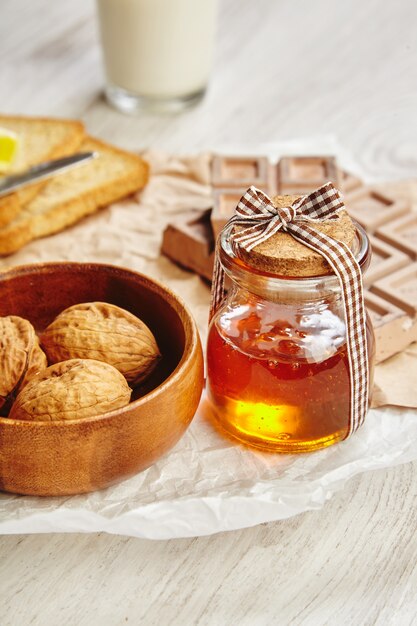 Nahes schönes Glas mit Honig mit Holzkappe geschnürt als Geschenk auf weißem Bastelpapier im Morgenlicht zum Frühstück.