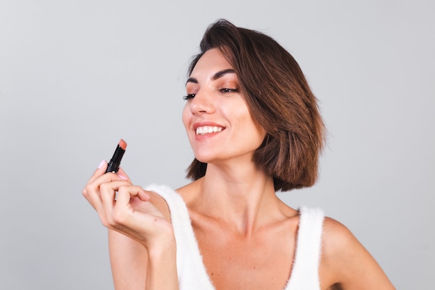 Nahes Schönheitsporträt der Frau mit Make-up und braunem Lippenstift auf grauer Wand