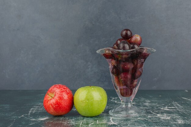 Nasse Äpfel und Glas schwarze Trauben auf Marmortisch.
