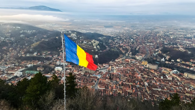 Nationalflagge auf der Spitze eines Hügels in der Nähe von Barsov kahle Bäume niedrige Wolken Stadtbild Rumänien