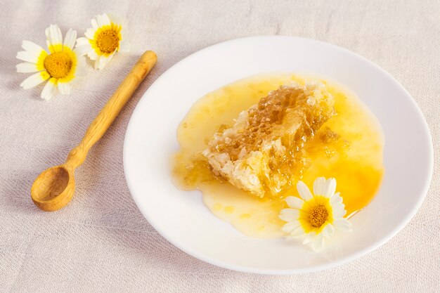 Natürliche Bienenwabe mit frischer weißer Blume und hölzernem Löffel