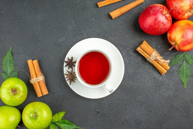 Natürliche organische frische äpfel mit grünen blättern, zimtlimetten und einer tasse schwarzem tee auf schwarzem hintergrund