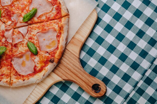 Neapolitanische Pizza mit dem Schinken, Käse, Rucola, Basilikum, Tomaten besprüht mit Käse auf einem hölzernen Brett auf einer Tischdecke in einer Zelle mit einem Platz für Text