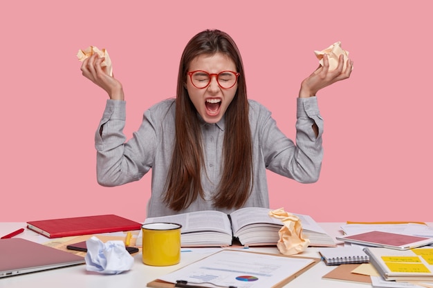 Kostenloses Foto negative emotionen, papierkram und studienkonzept. empörte schöne dame runzelt die stirn, schreit laut