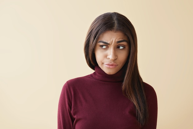 Negative menschliche Gefühle und Emotionen. Porträt einer unzufriedenen jungen dunkelhäutigen Frau, die nach dem Streit mit ihrem Mann stilvoll die Stirn runzelt und schmollt, sich beleidigt und gestresst fühlt