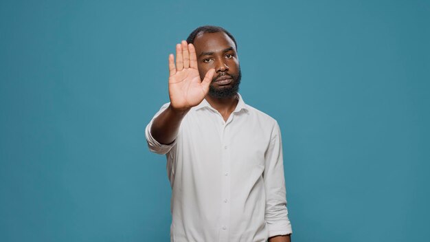 Negative Person, die im Studio ein Stoppsymbol mit der Handfläche macht und Leugnung und Ablehnung ausdrückt. Junger Mann, der die Idee ablehnt und missbilligt, die Hand hebt, um den Vorschlag abzulehnen und abzulehnen.