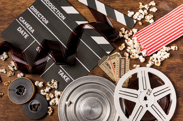 Negative Streifen mit Filmklappe; Filmrollen; Karten und Popcorn auf hölzernem Schreibtisch