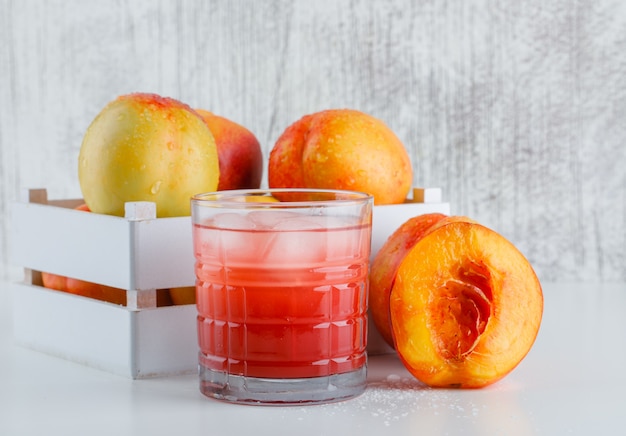 Kostenloses Foto nektarinen in einer holzkiste mit saft-seitenansicht auf weißer und schmuddeliger wand