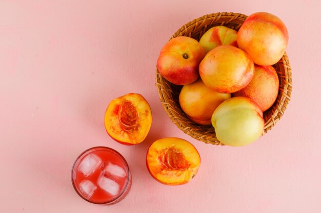 Nektarinen mit Saft in einem Korb auf rosa Oberfläche, flach liegen.