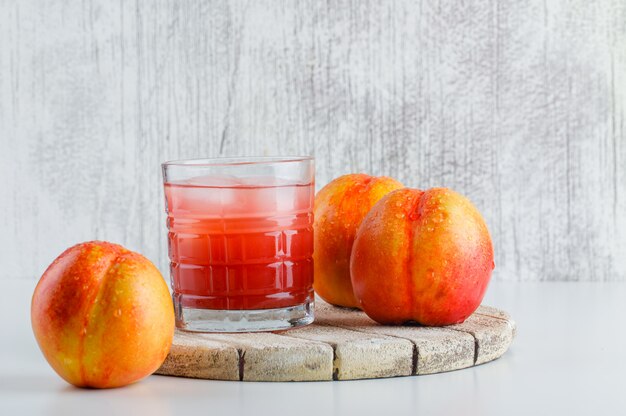 Nektarinen mit Schneidebrett, Saft auf weißer und schmuddeliger Wand, Seitenansicht.