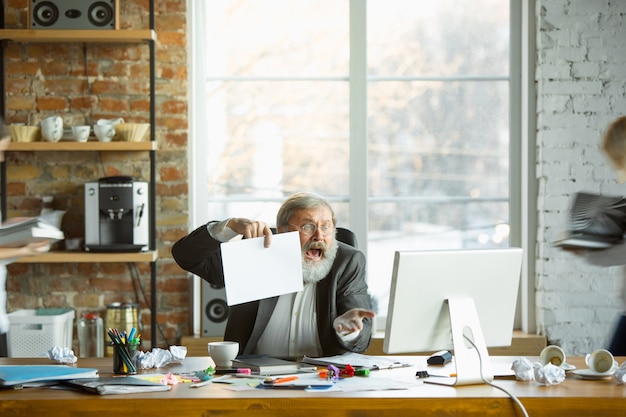 Nervöser und müder Chef an seinem Arbeitsplatz beschäftigt, während Leute, die sich nähern, verschwimmen. Büroangestellter, Manager, hat Probleme und Fristen, seine Kollegen lenken ab. Business-, Work-, Workload-Konzept.