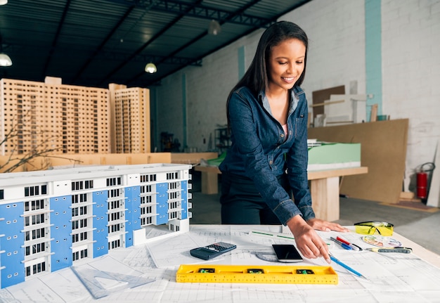Nette afro-amerikanische Dame, die nahes Modell des Gebäudes auf Tabelle steht