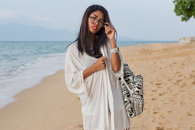 Nette asiatische Frau des Reisenden im weißen Kleid, das auf dem tropischen Strand geht. Hübsche Frau, die Urlaub genießt