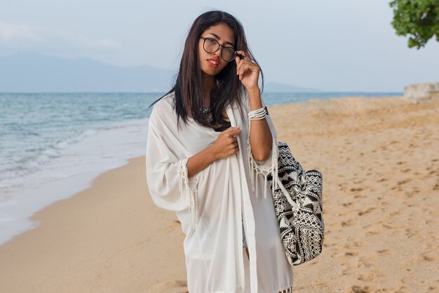 Nette asiatische Frau des Reisenden im weißen Kleid, das auf dem tropischen Strand geht. Hübsche Frau, die Urlaub genießt