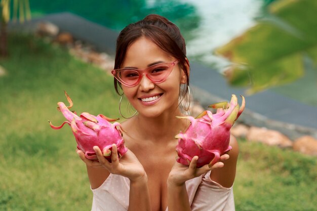 Nette asiatische Frau, die rosa Drachenfrüchte in den Händen hält