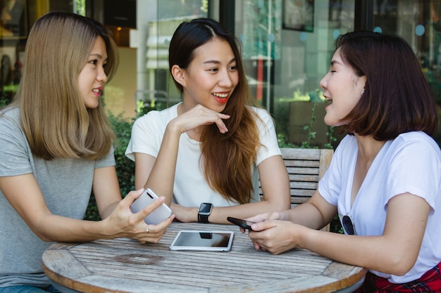 Nette asiatische junge frauen, die in trinkendem kaffee des cafés mit freunden sitzen und zusammen sprechen