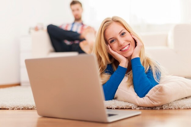 Nette blonde Frau, die mit Laptop auf Teppich zu Hause entspannt