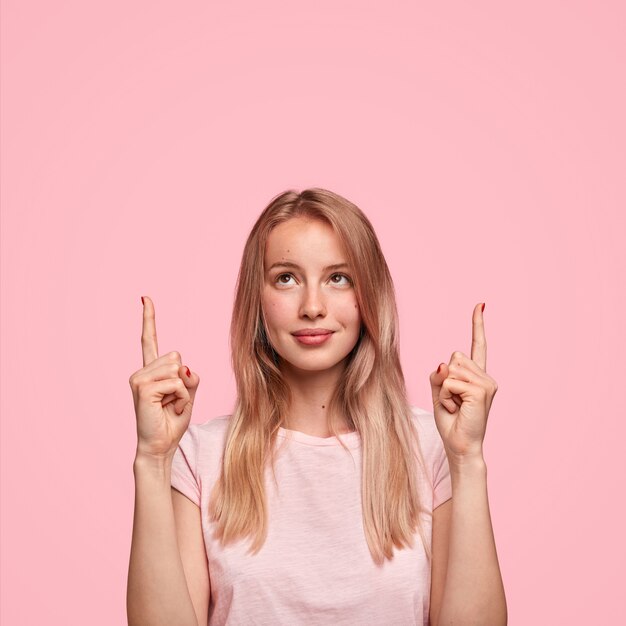 Nette blonde Frau mit langen Haaren, zeigt mit zwei Vorderfingern nach oben