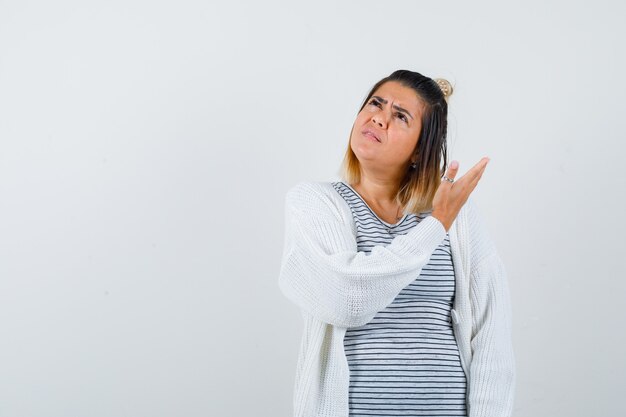 Nette Dame, die etwas oben zeigt, in T-Shirt, Strickjacke nach oben schaut und verwirrt aussieht, Vorderansicht.