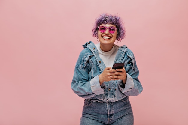 Nette erwachsene Dame mit hellem Haarschnitt in der Sonnenbrille lacht. Lächelnde Frau mit dem lockigen Haar, das Telefon hält.