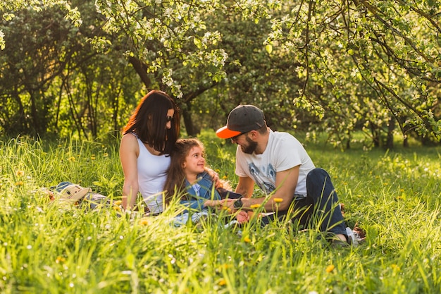 Nette Familie, die auf Gras im grünen Park sitzt