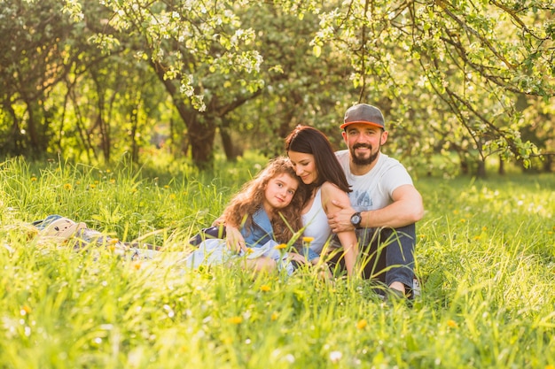 Nette Familie, die im grünen Gras während des Sommers sitzt