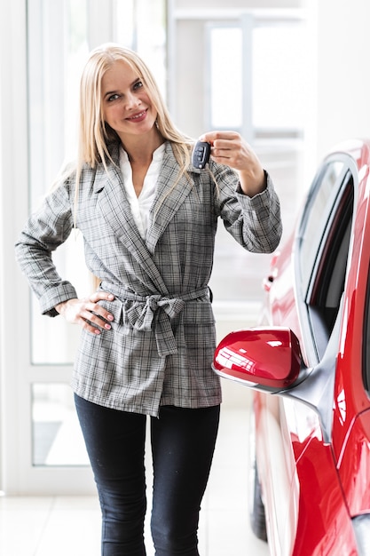 Nette frau, die an den schlüsseln des autos darstellt und die kamera betrachtet