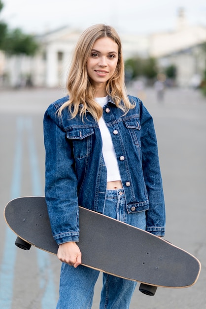 Nette Frau, die eine Skateboard-Vorderansicht hält