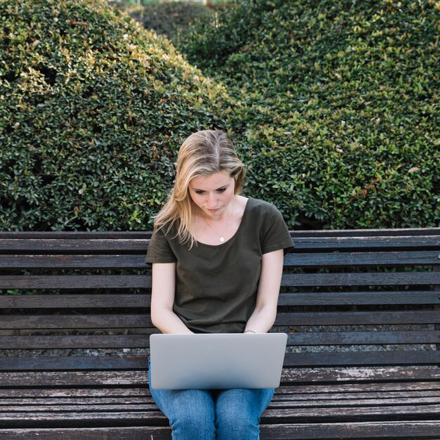 Nette Frau, die Laptop auf Bank verwendet